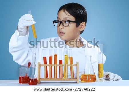 Young asian little scientist looking at chemical fluid over blue background