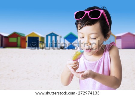 Closeup of little child eats a melt ice cream on the shore while wearing swimwear