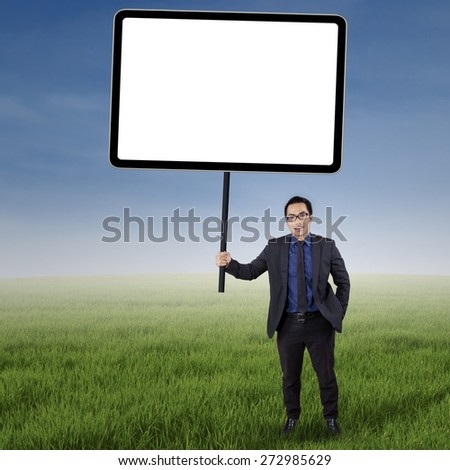 Portrait of male worker in business suit, standing on the meadow while holding an empty board