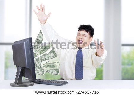 Cheerful male worker celebrate his success while working in the office and get money from internet