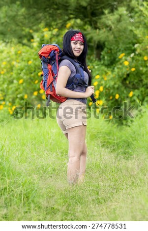 Rear view of beautiful woman carrying backpack while walking in the forest and smiling at the camera