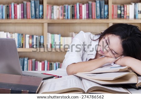 Portrait of teenage schoolgirl sleeping above textbooks on the table in the library