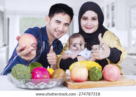 Healthy family showing thumbs-up in the kitchen with fresh fruits on the table