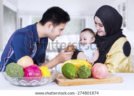 Portrait of healthy family with fresh fruits in the kitchen, man give fruit to his son