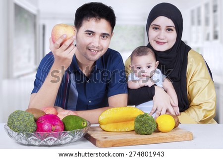 Portrait of two parents sitting at home with their little son and fresh fruit on the table