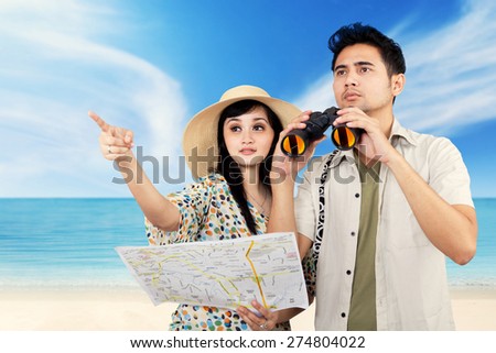 Portrait of two young asian tourists sightseeing on the beach while carrying a map and binoculars