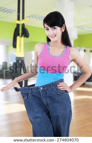 Attractive young woman showing her old jeans at the gym center after doing lose weight program