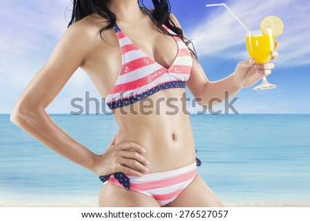 Attractive female model wearing sexy swimsuit on the coast while holding a fresh drink