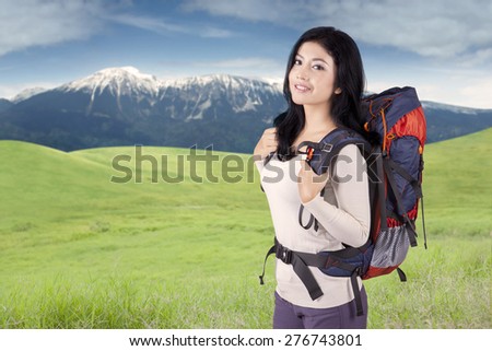 Portrait of happy woman ready for hiking, standing on the mountain while carrying backpack
