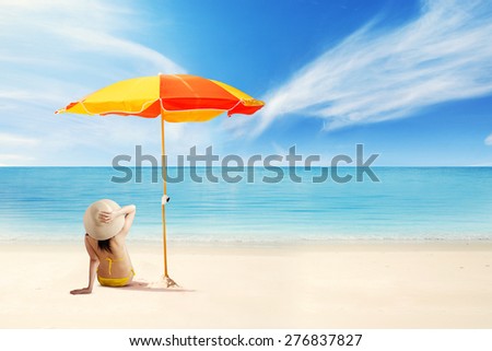 Rear view of young woman enjoy holiday by sightseeing on the beach and sitting under umbrella