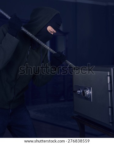 A burglar with a crowbar is trying to open a safe at home