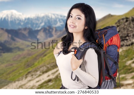 Portrait of beautiful female hiker smiling on the camera while carrying backpack on the edge of the mountain
