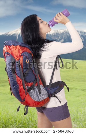 Portrait of female hiker carrying backpack and take a break while drinking fresh water from the bottle