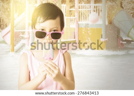 Portrait of happy little girl standing at the pool while wearing sunglasses and enjoy ice cream, shot with an instagram effect