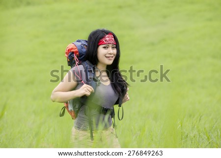 Attractive female backpacker smiling on the camera while carrying backpack and walking on the mountain