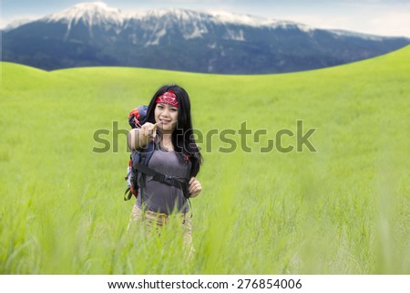 Beautiful woman carrying backpack while walking on the meadow and pointing at camera