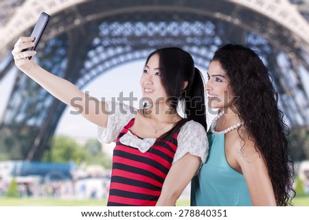Joyful multi ethnic girls taking self photos using mobile phone near the Eiffel Tower