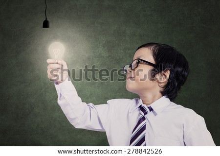 Smart asian child holding a lit bulb under lamps