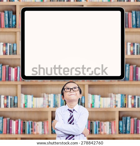 Male little student thinking idea in the library while looking up at the empty board