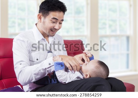 Portrait of young man sitting on couch at home while change his baby clothes