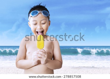 Portrait of cute naked little boy enjoying cool ice cream while wearing swimming glasses on the beach