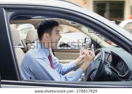 Young businessman driving a car and looks angry, showing two middle fingers and screaming