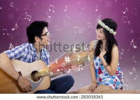 Portrait of happy couple singing and playing guitar together, shot with a purple bokeh background