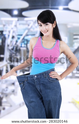 Portrait of successful woman lose her weight, standing at gym center with her old jeans