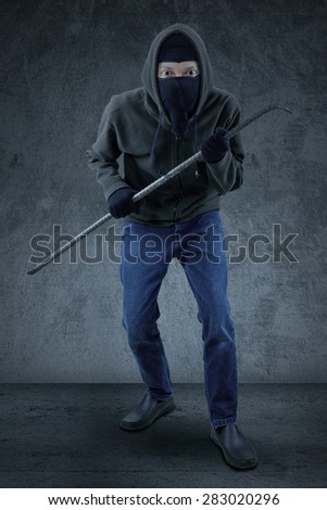 Male mugger wearing black jacket and mask, ready to action while carrying a crowbar