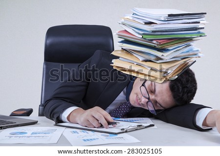 Caucasian entrepreneur sleeping on the tablet with a pile of paperwork on his head