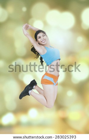 Joyful healthy woman wearing sportswear and jumps with light glitter background