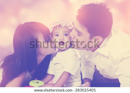 Portrait of two parents kiss their little daughter with defocused lights background