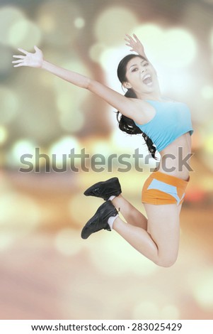 Attractive woman with sportswear, jumping with light glitter background