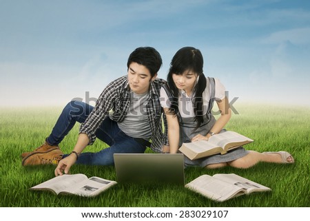 Young couple sitting on grass while studying with laptop