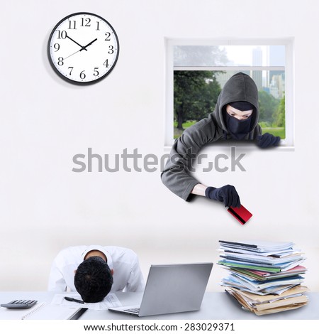 Male burglar wearing mask and stealing a credit card in the office through a window