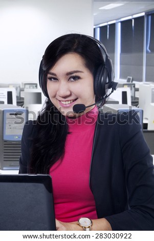 Attractive female call center operator working in the office room and smiling at camera