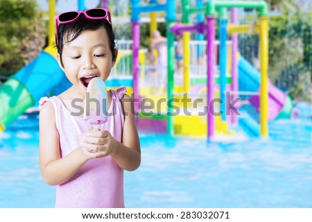 Closeup of beautiful little girl wearing bikini at pool while eating ice cream