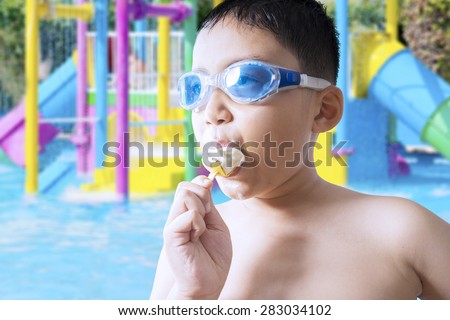 Closeup of male child wearing swimming glasses on the pool while enjoying a delicious ice cream