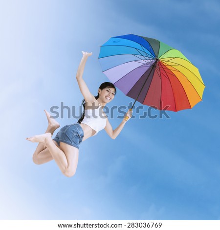 Attractive young girl enjoy summer holiday and jumps with a colorful umbrella under clear sky