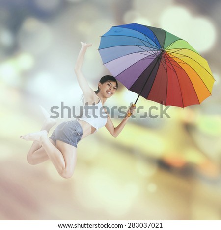 Cheerful young woman with colorful umbrella and jumps over light glitter background