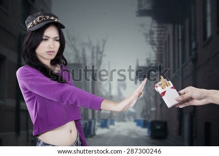 Portrait of modern teenage girl showing her hand and refuse to smoke, shot on the alley
