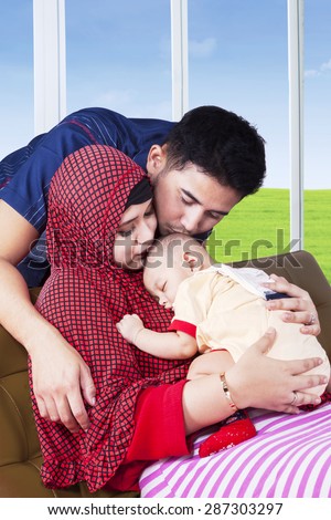 Two happy muslim parents kiss their baby while sleeping on the mother\'s chest, shot at home