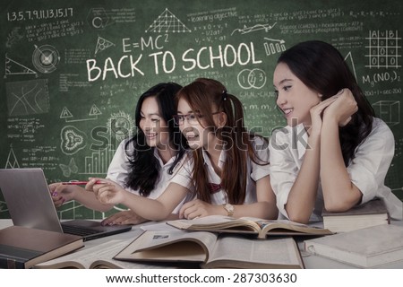 Portrait of beautiful female students studying together and pointing at the laptop in class