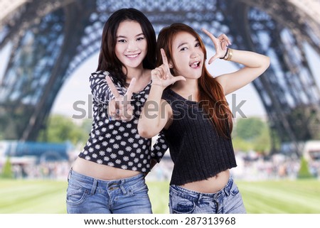 Two teenage girls enjoy holiday in the Eiffel Tower and look at the camera with funny poses