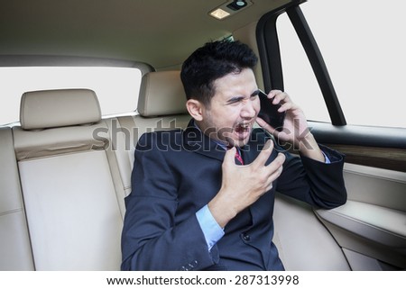 Young entrepreneur sitting on the back side while scolding someone on the phone in the car
