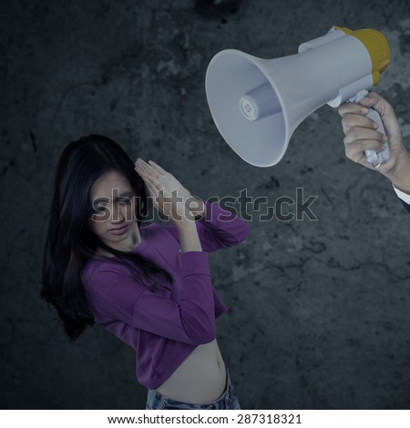 Portrait of teenage girl scolded with a megaphone by someone and looks scared