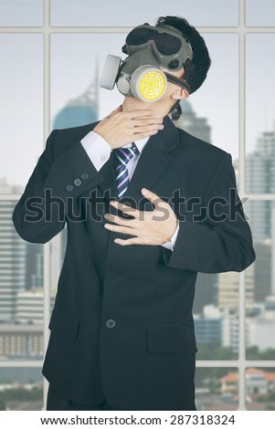 Male entrepreneur standing in the office with gas mask and getting heart attack