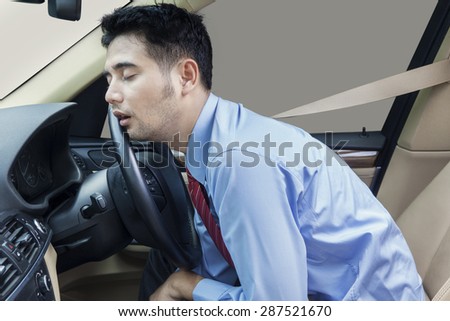 Young businessman driving a car and looks tired, sleeping in the car while wearing the safety belt