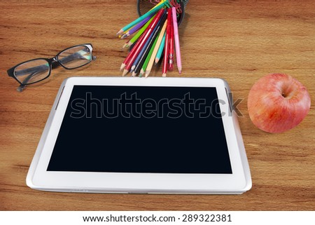 Tablet PC with glasses, stationery, and apple on wooden background