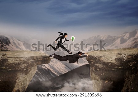 Female entrepreneur get a help from her partner for through a cliff on mountain